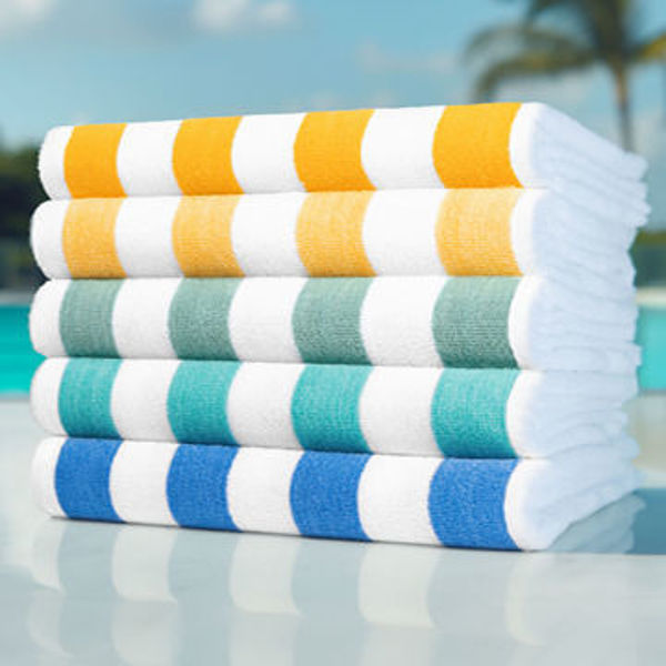 Five Oxford Playa 2x2 Cabana Pool Towels by Ganesh Mills, featuring wide horizontal stripes in yellow, green, teal, and blue, are stacked poolside with palm trees and a blue sky in the background.