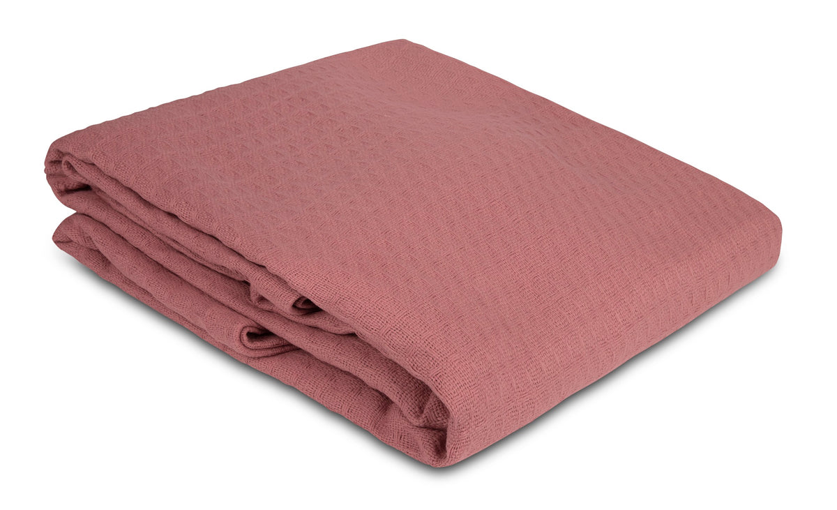 A folded, textured dusty rose KSE Waffle Weave Blanket is displayed on a white background, emphasizing the cozy appeal and quality cotton construction of KSE’s Waffle Weave Blankets.