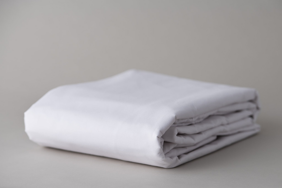 A neatly folded Healthcare sheet - T-180 Impressions Print by Thomaston Mills lies on a light gray surface with a soft, neutral background, evoking the crisp quality of economy hotel linens.