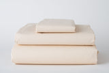 A neatly folded stack of Thomaston Mills Fitted Sheets Deep Pocket Hospitality - Single Pick Percale, in light beige, including fitted sheet, flat sheet, and pillowcase—perfect for commercial laundry or hospitality bedding.