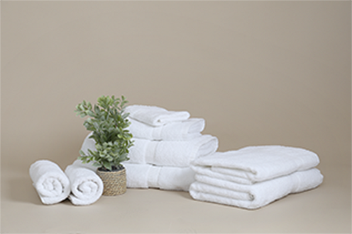A set of KSE Excellence Collection Hotel hand towels, both folded and rolled, is arranged neatly beside a small potted plant against a plain beige background.
