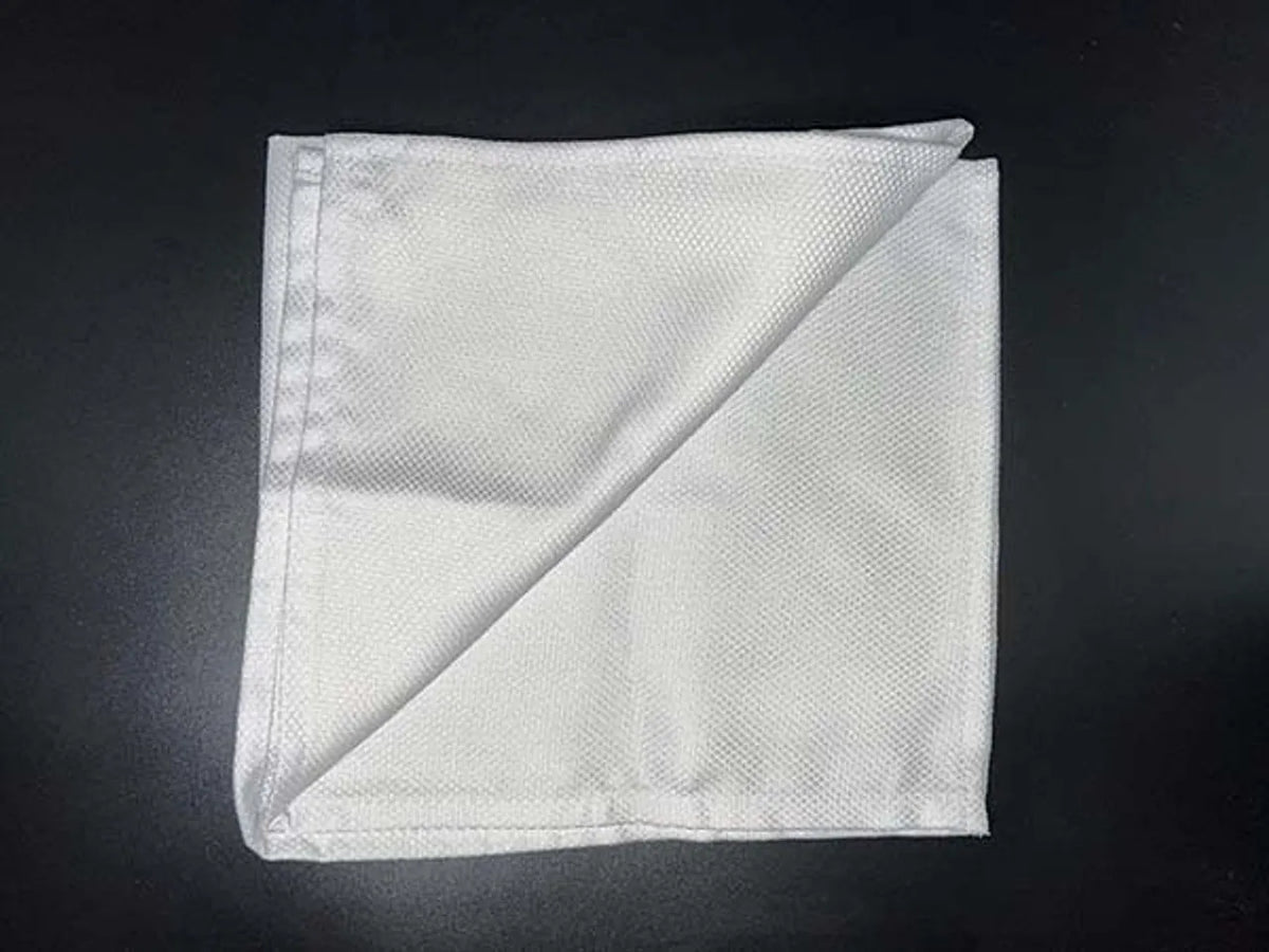 A neatly folded Ganesh Mills Bird Eye Napkin in white/black spun polyester, featuring a subtle birds eye texture and an inward-folded corner that displays both fabric sides against a dark background.
