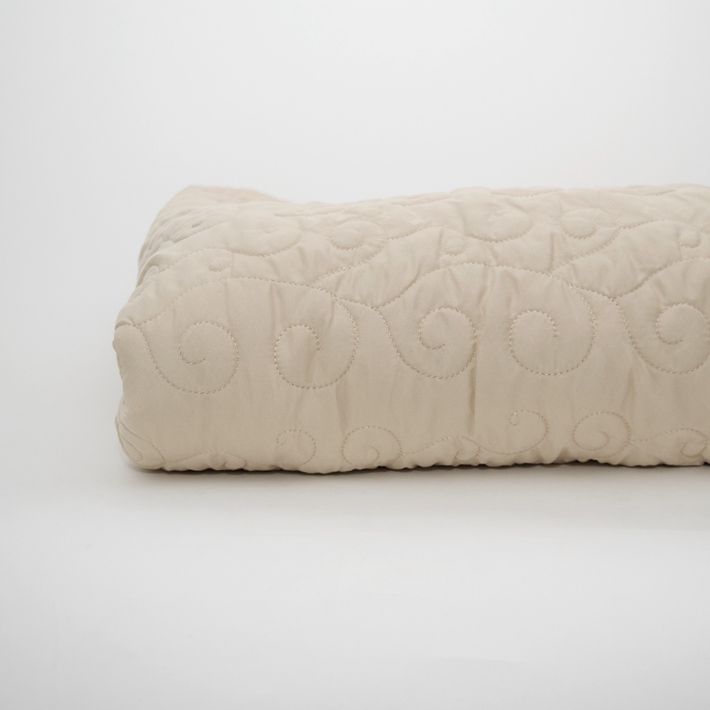The Calderon Textiles Ascent Standard Bedspread, in beige with subtle swirl quilting, is neatly folded and displayed on a plain white background.