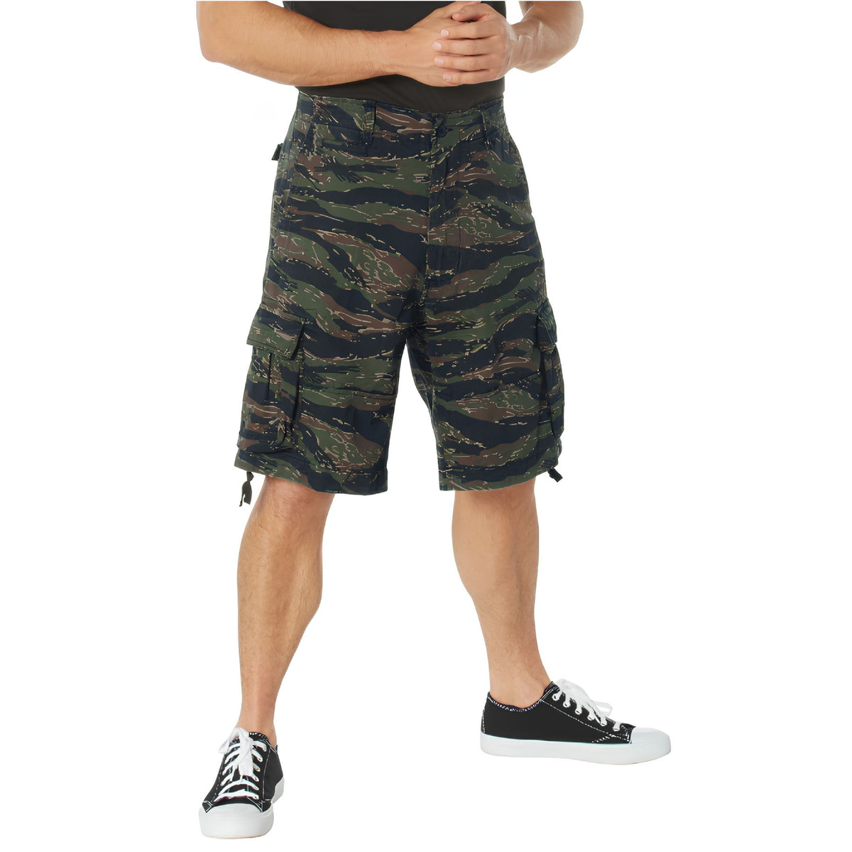 A person stands with hands clasped, wearing a black shirt, Rothco Vintage Infantry Utility Cargo Shorts by Rothco, and black-and-white sneakers. The image is cropped from the shoulders down.