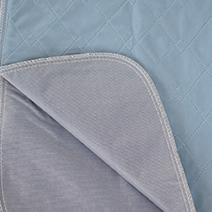 A close-up of a blue quilted Calderon Textiles Underpad Vinyl Lining with stitched diamond patterns, folded to show its smooth light gray underside and white-stitched edging—an example in the 34 x 36 underpads range.