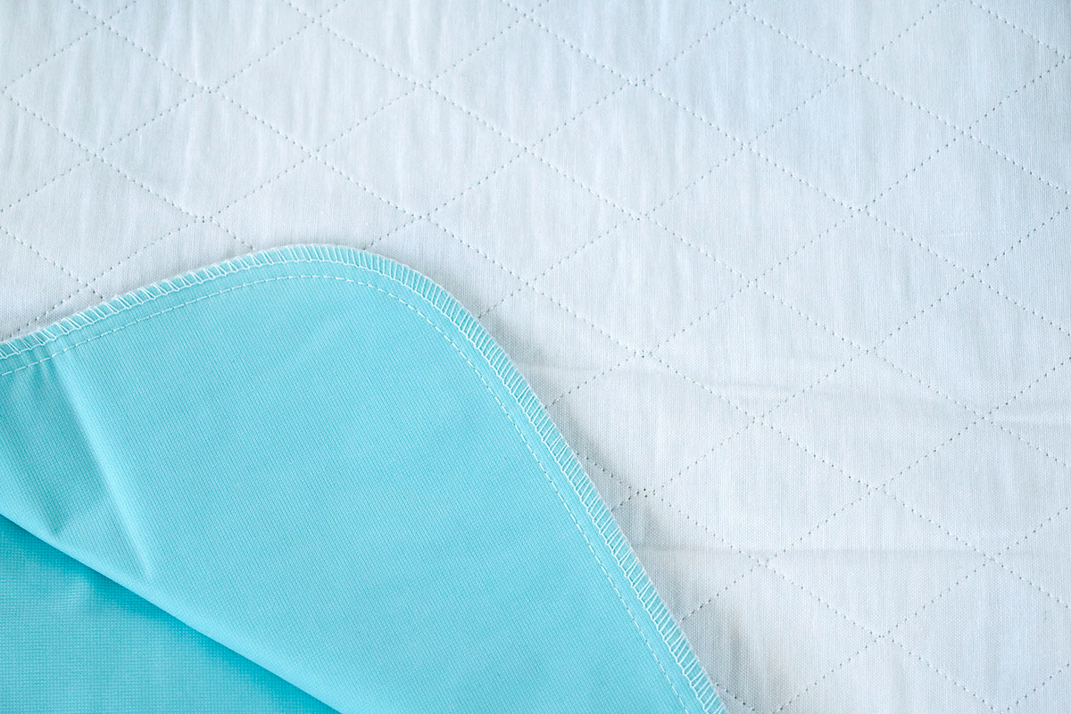 A close-up of Calderon Textiles Underpad Vinyl Lining shows the quilted white surface and light blue waterproof underside with detailed stitching—perfect for those seeking 34 x 36 underpads and top underpad performance.