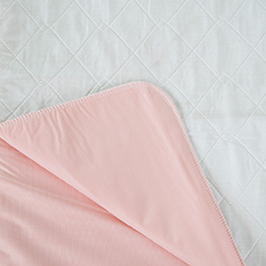 A pale pink blanket with a textured edge is partially folded back on a white quilted surface, revealing Calderon Textiles Underpad Vinyl Lining (34 x 36), competitively priced and designed for superior underpad performance.