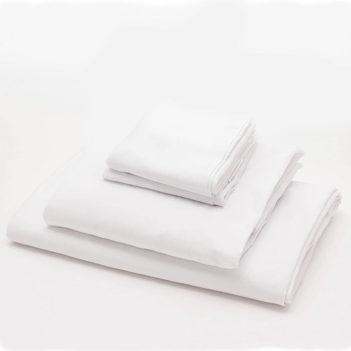 A neatly folded stack of plain white Pillowcase USA Bedding-Berry compliant from Berry Compliant is placed on a white surface, creating a clean and minimalist look.