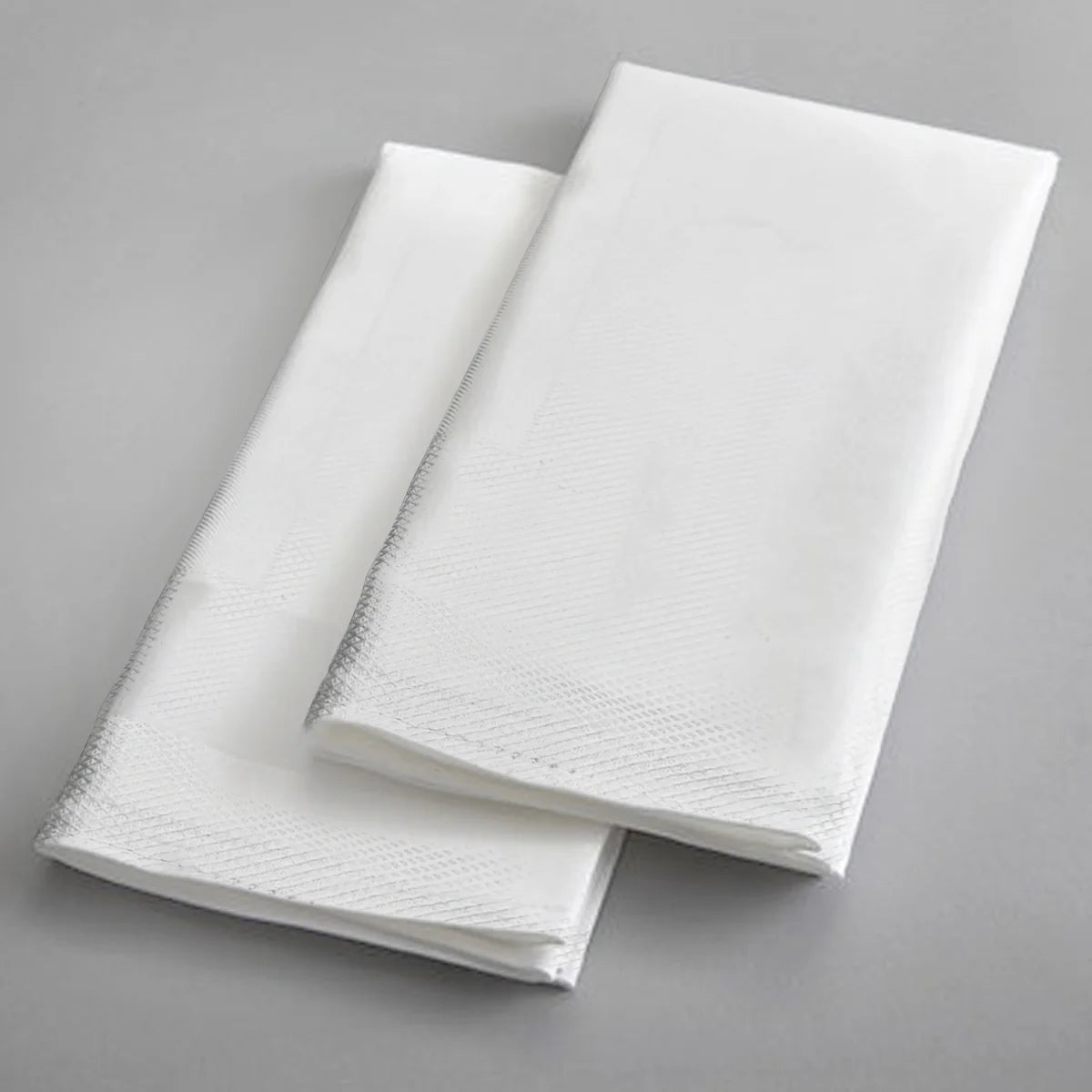 Two Ganesh Mills Napkins - 4 Sided Hemmed White Bird Eye Banquet Table Linen are neatly folded and placed parallel on a light gray surface, showcasing their subtle textured edge patterns.