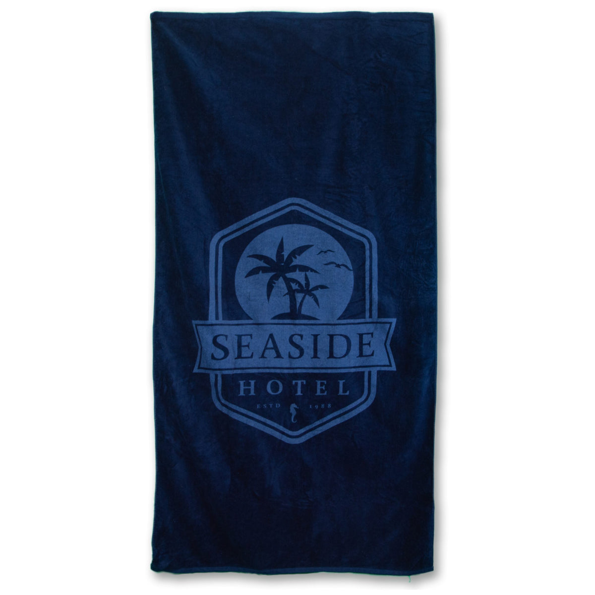 The Pro Towels Beach Towel - Platinum Collection is a dark blue heavyweight cotton towel featuring a centered Seaside Hotel logo with palm trees, birds, and an anchor.