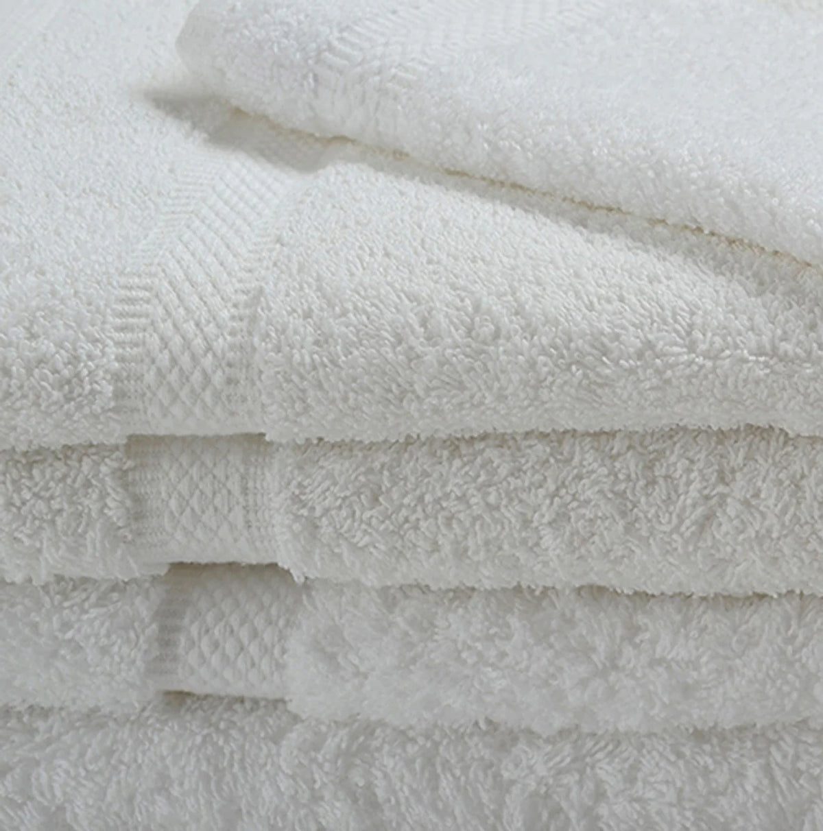 A close-up of neatly stacked Ganesh Mills White Oxford Imperiale Hand Towels, featuring a textured edge pattern.