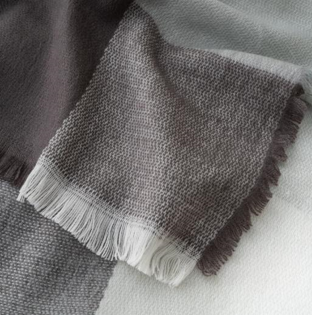 The Canyon Comfort Throw by Pro Towels features a woven gray plaid design with checkered patterns and fringed edges. Its visible texture highlights the soft, cozy fabric, making it a perfect accent for any space.