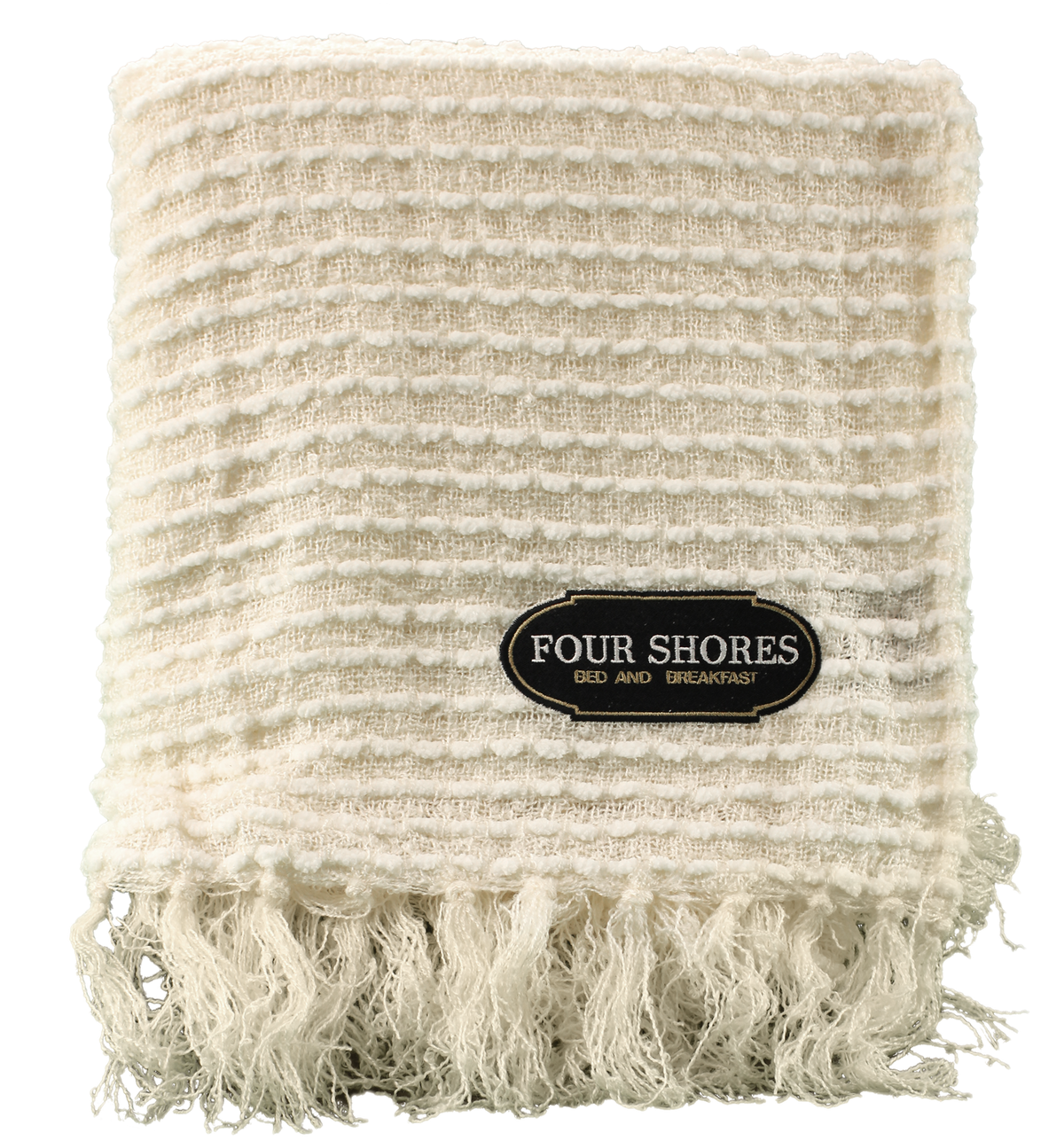 The cream-colored, textured Charleston Throw by Pro Towels features fringed edges and custom embroidery on a label reading Four Shores Bed and Breakfast.
