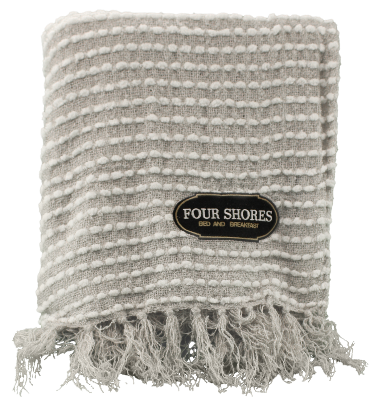The Charleston Throw by Pro Towels is a gray and white textured blanket with fringe at the bottom and custom embroidery featuring a Four Shores Bed and Breakfast patch on the front.
