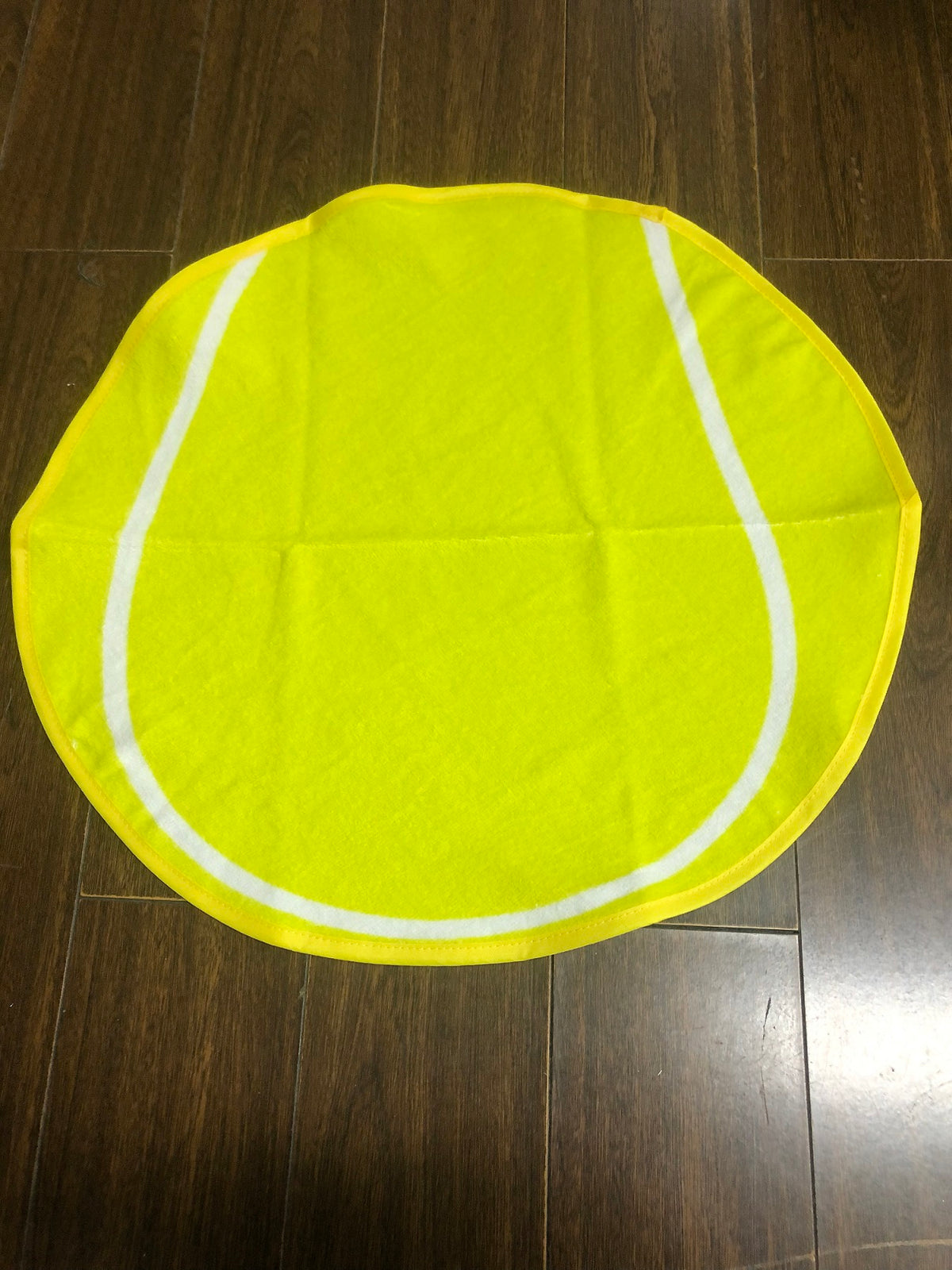 A Tennis Ball Shaped Sport Towel by Pro Towels, featuring a fiber reactive yellow design with white curved lines, is displayed on a dark wooden floor.