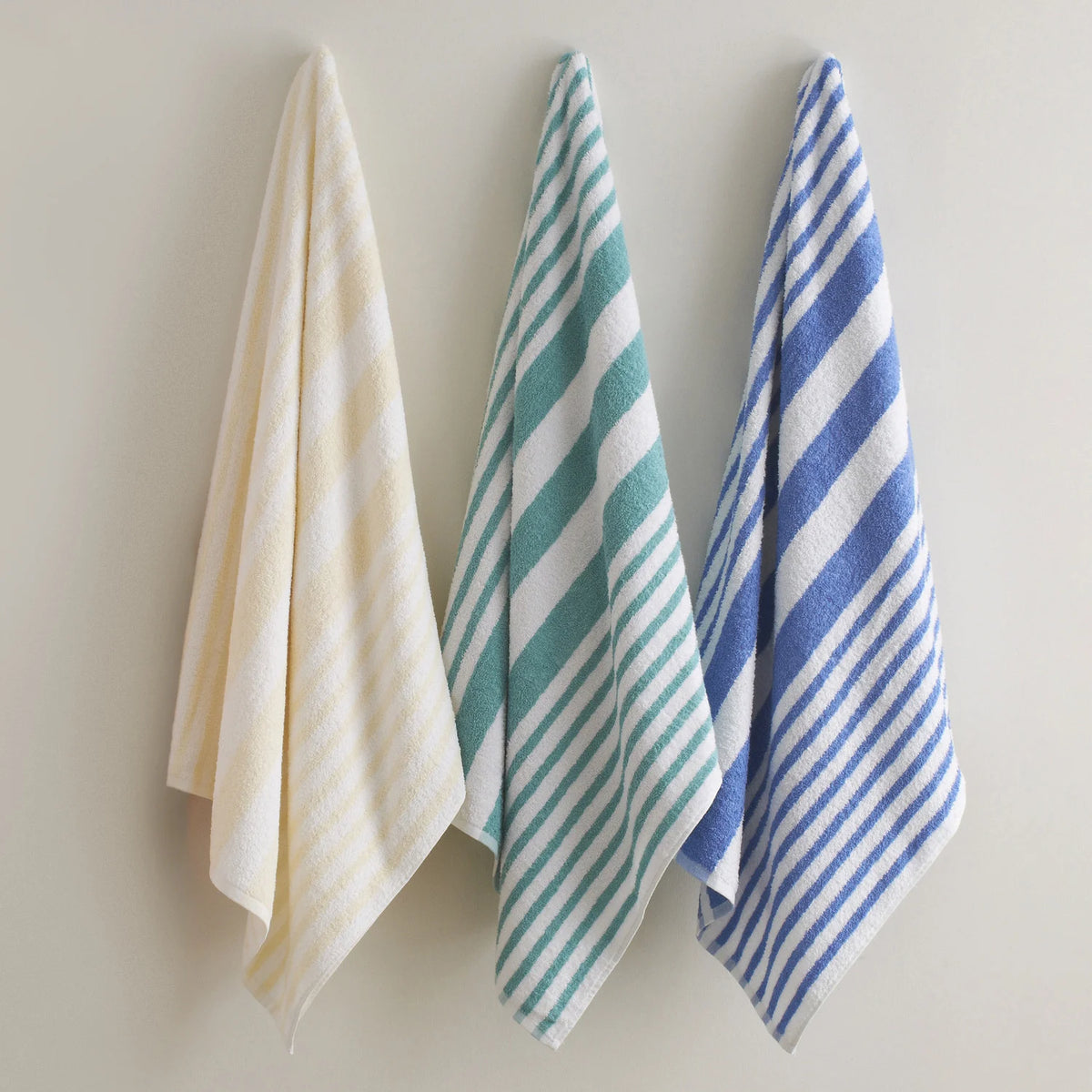 Three towel sets with beige, teal, and blue and white stripes on a neutral background.