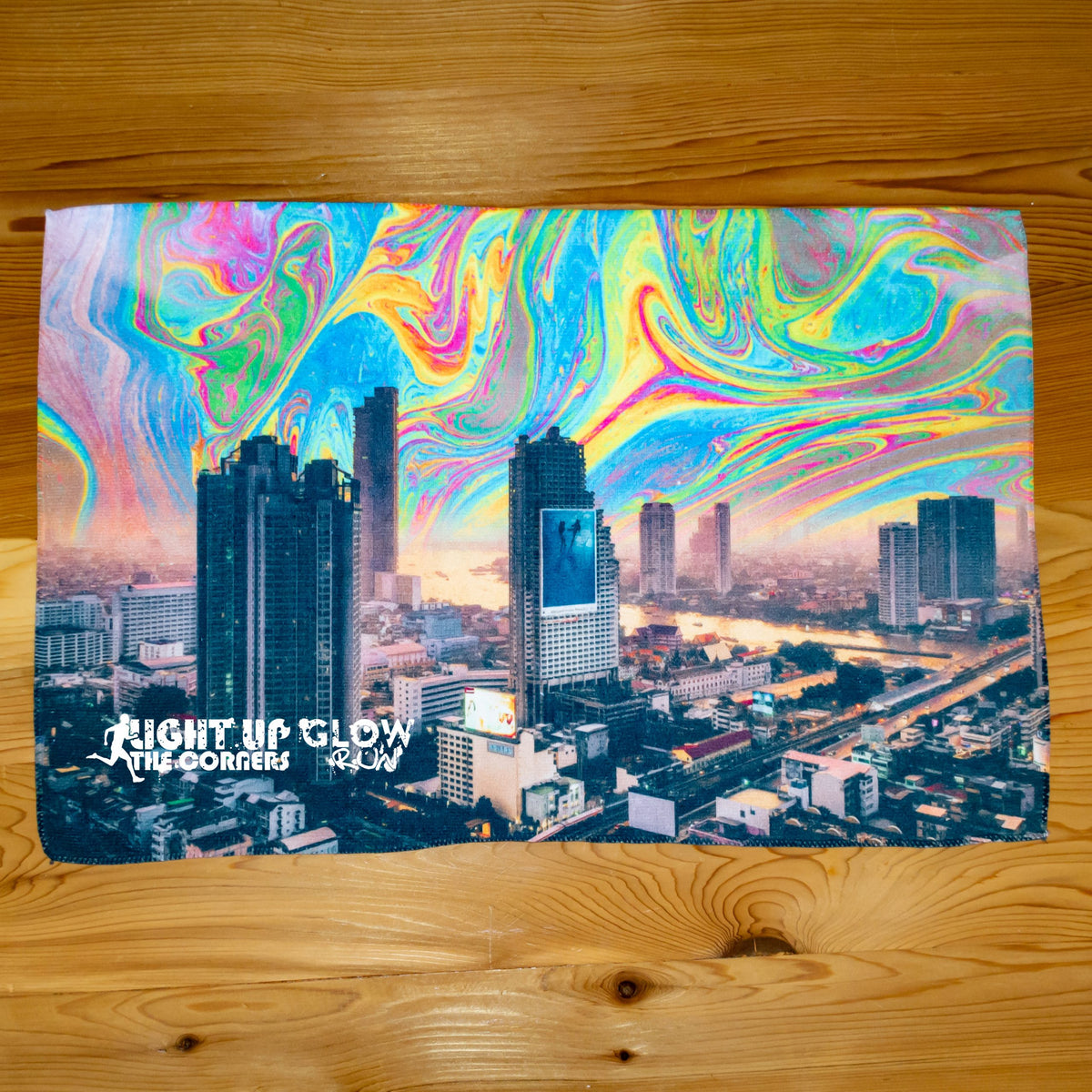 A vibrant city skyline and river with a swirling rainbow sky, overlaid text reading LIGHT UP GLOW THE CORNERS RUN. Ideal as a sublimation-ready design for the Pro Towels Microfiber Sports Towel—perfect for eye-catching promotions.