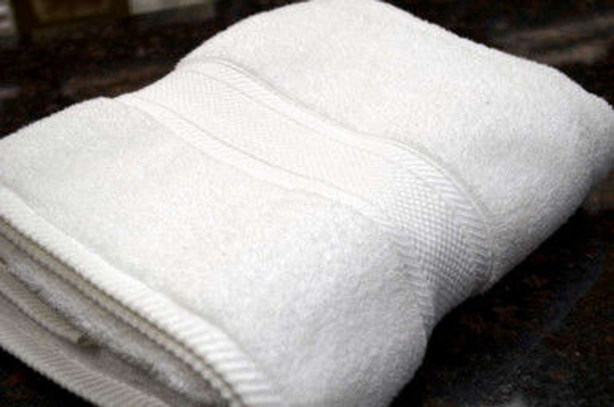 The Bulk Linen Supply Bath Sheet / Pool Towel - White Oxford Miasma Towel, featuring textured bands and luxury hotel style, is neatly folded on a dark, reflective surface.