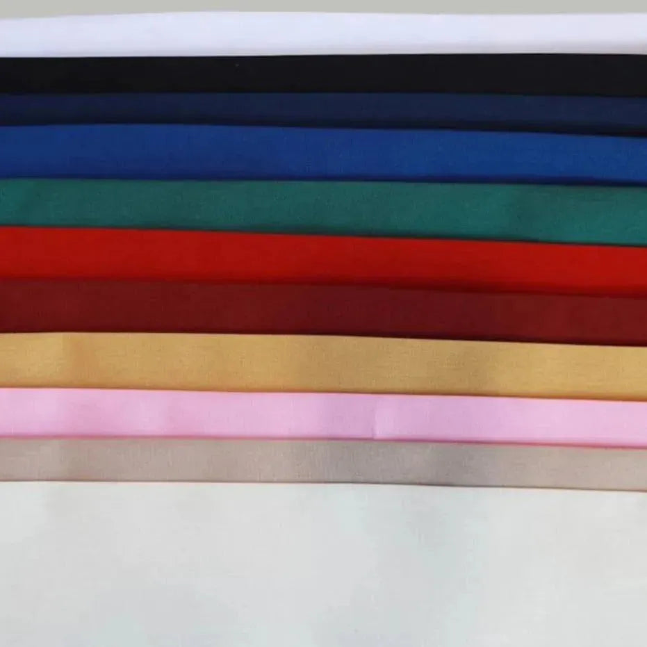 A stack of Ganesh Mills Napkins - 100% Spun Economy Cloth in assorted solid colors—white, black, blue, green, red, brown, yellow, pink, and beige—neatly arranged for convenient bulk napkin use.