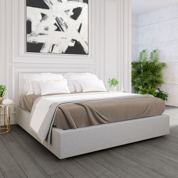 A modern bedroom with a low grey upholstered bed features crisp white bedding, Ganesh Mills Oxford Polar Fleece Blanket in beige, and white pillows. A large abstract black-and-white painting hangs above the bed, with green plants and a round bedside table adding charm.