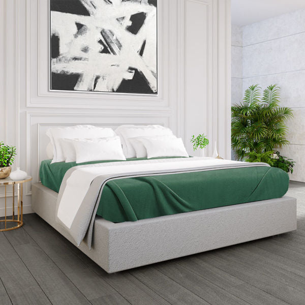 A modern bedroom with a gray upholstered bed, white bedding, Ganesh Mills Oxford Polar Fleece Blanket (anti-pilling, double stitched), black-and-white wall art, potted plant, white paneled walls, and dark wood floor.