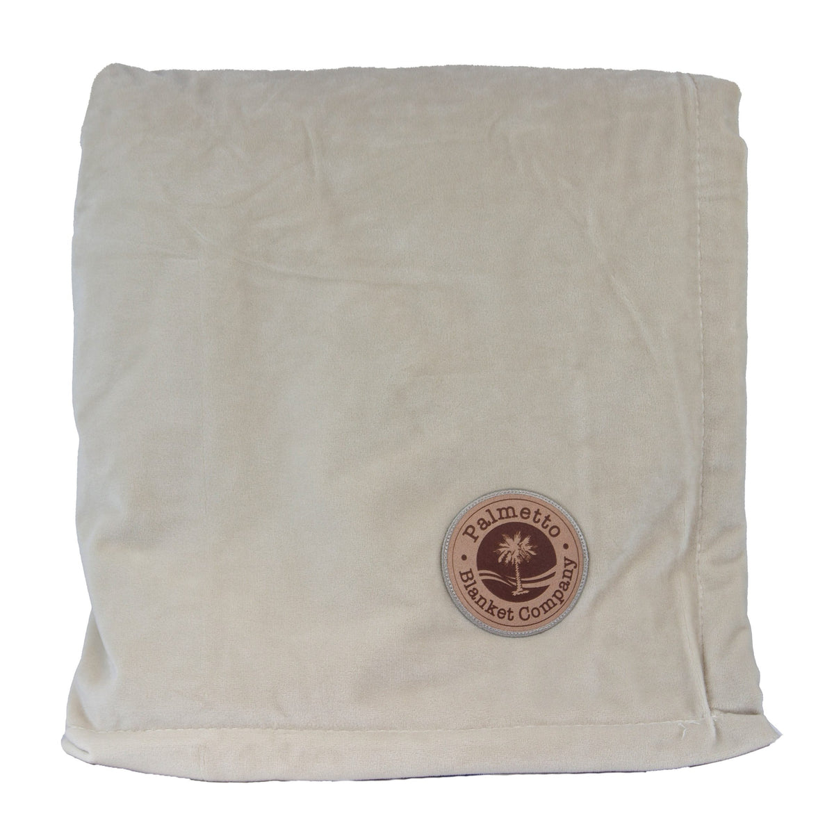 A folded beige Opulence Throw blanket from Pro Towels features a round brown patch in the corner with a palmetto tree logo and text—ideal for custom embroidery or as a cozy home accent.