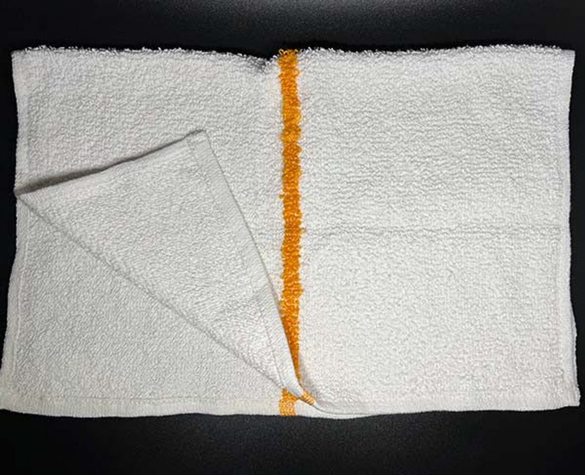 A white rectangular Ganesh Mills dishcloth from the Oxford Cleaning Towels & Bar Mops line, featuring a single vertical orange stripe, lies on a dark surface with one corner folded to show its texture and underside.