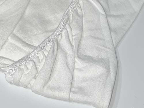 A close-up of the Ganesh Mills Oxford Baby Crib Sheet with 4" Pocket in premium cotton, featuring elastic edges and gathered fabric, laid flat to showcase its detailed texture and stitching.