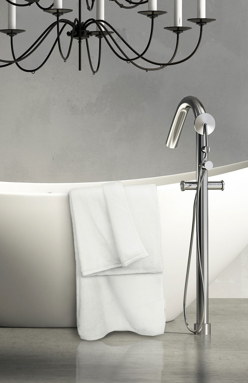 A modern bathroom features a white freestanding tub with a Ganesh Mills Washcloth - White Oxford Platinum Towel draped over the side, a sleek chrome floor-mounted faucet, and a black metal chandelier against a gray wall.