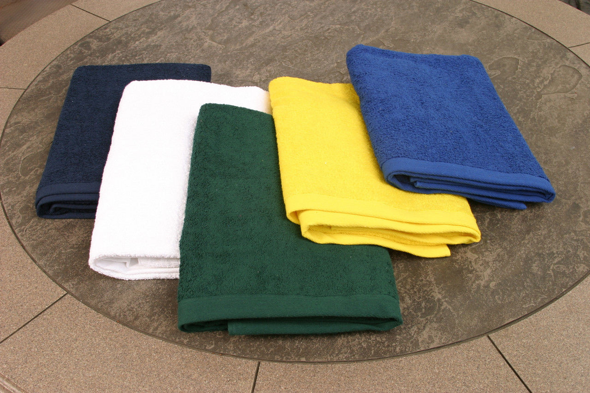 Five folded Ganesh Mills Oxford B2700 Premium Pool Towels in navy, white, green, yellow, and royal blue are neatly stacked on a round stone table. Made from ringspun cotton, they bring luxury to your pool or beach day.