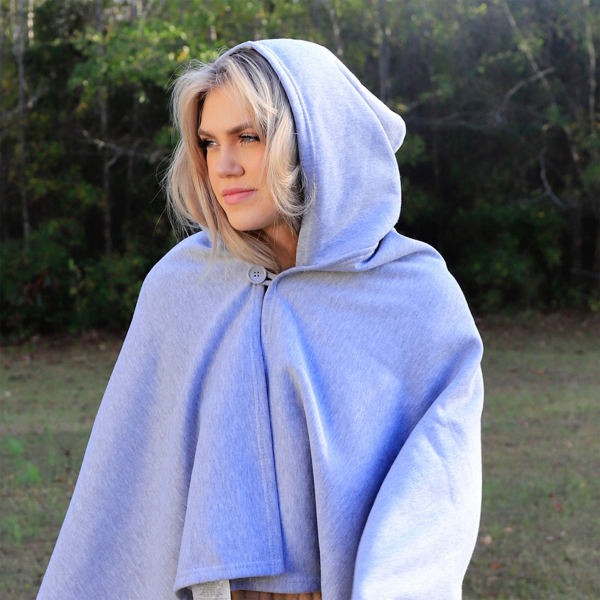 A woman with blonde hair wears the Pro Towels Sweatshirt Sport Hoodie in light gray, standing outdoors among trees and greenery, gazing thoughtfully to the side.