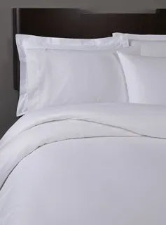 A neatly made bed with the 1Concier Flat Sheet T300 100% Cotton Sateen exudes luxury, its crisp white bedding set elegantly contrasting with a dark wooden headboard.
