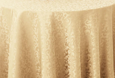 A round table draped with the Oxford Round Table Linen - Multicolor by Ganesh Mills, showcasing a swirling, ornate pattern.