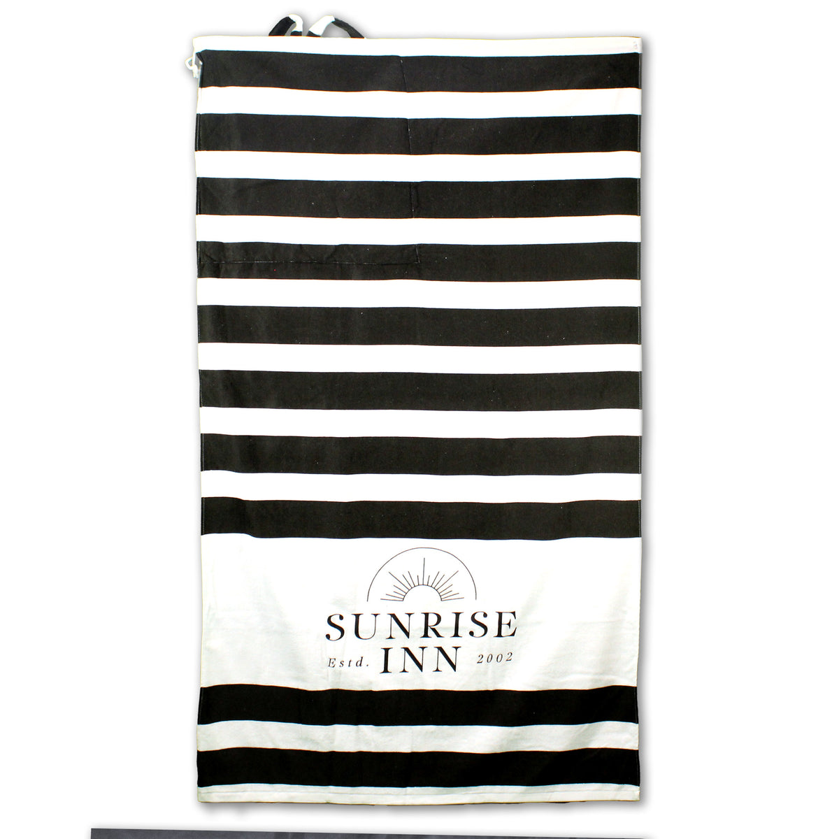 The Shore Buddy - Striped Cabana Beach Towel by Pro Towels is a rectangular cotton towel with black and white stripes, "SUNRISE INN Estd. 2002," and a sun graphic printed near one end.