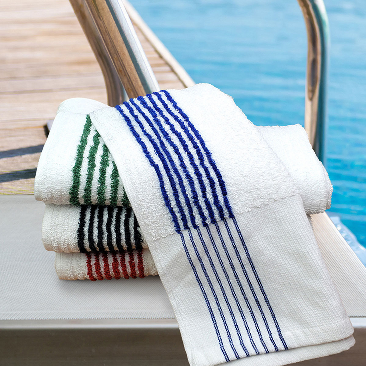 The Oxford Super Gym Towels by Ganesh Mills—white with 8 color stripes—are neatly stacked on a poolside lounge chair, ideal for gyms, fitness centers, or home use. Bleach-proof and durable for bulk purchase.