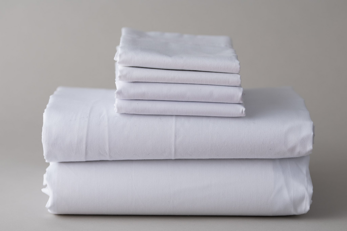 A neatly folded stack of Thomaston Mills Healthcare Items - T-180 Jade Green sheets and pillowcases arranged on a neutral surface with a plain, light-colored background.