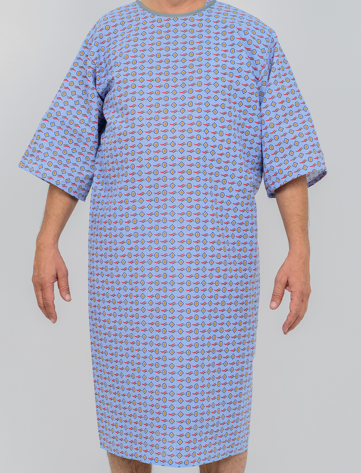 A person is shown from the neck down wearing a KSE Three-Arm hole Gown, featuring a blue pattern and short sleeves, against a plain light background. The individual’s face is not visible.