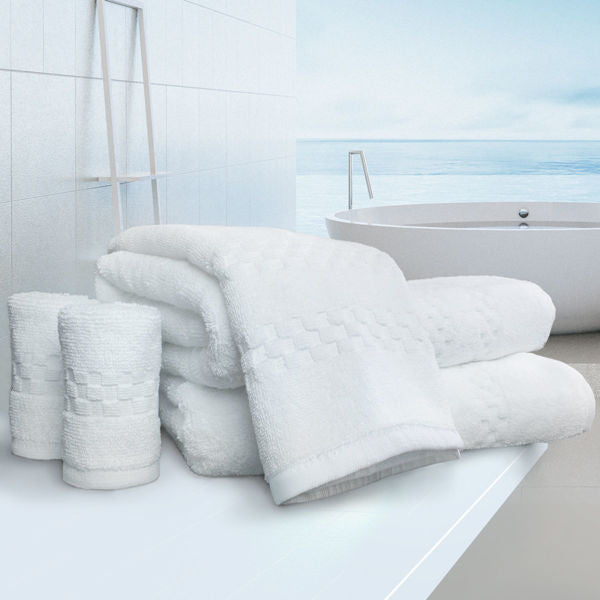Three neatly rolled luxury bath towels and two folded Ganesh Mills Hand Towel - White Oxford Viceroy Towels are arranged on a bathroom counter near a round tub, with water views through large modern windows.