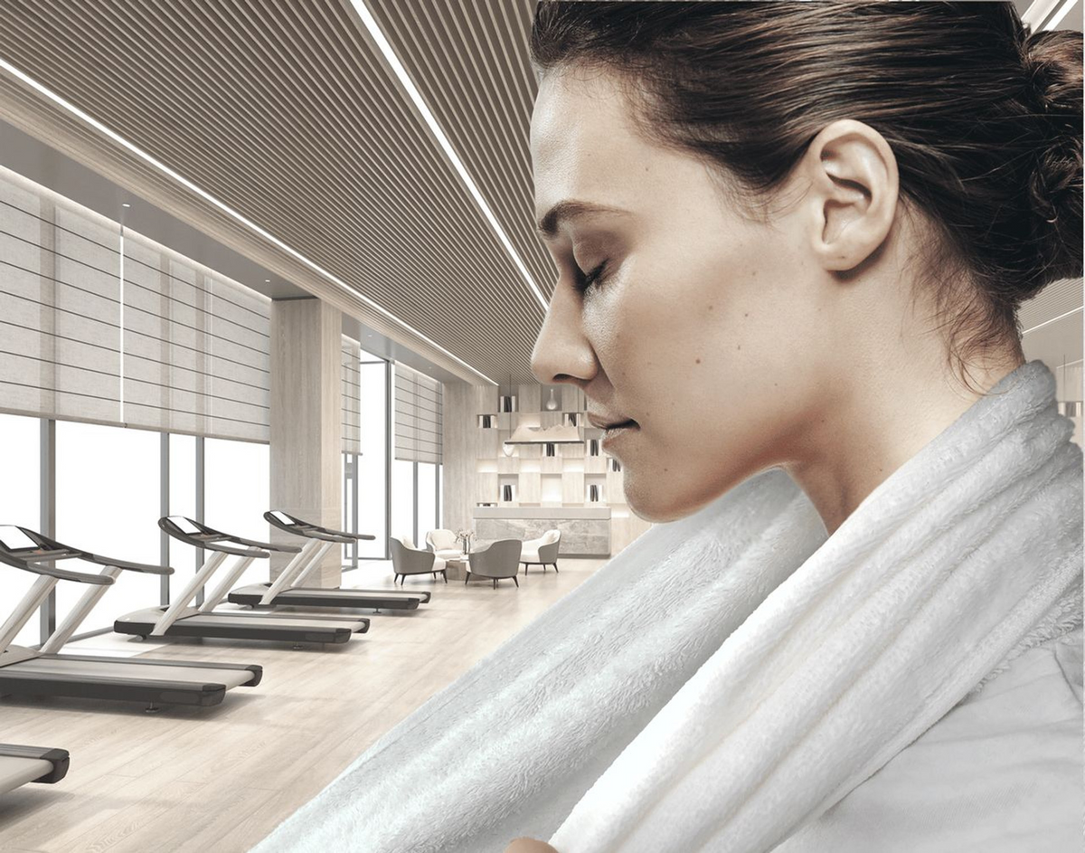 A woman with closed eyes wears a Ganesh Mills Sports Neck Towel Hemmed - White Velour in a modern gym, surrounded by treadmills and large windows.