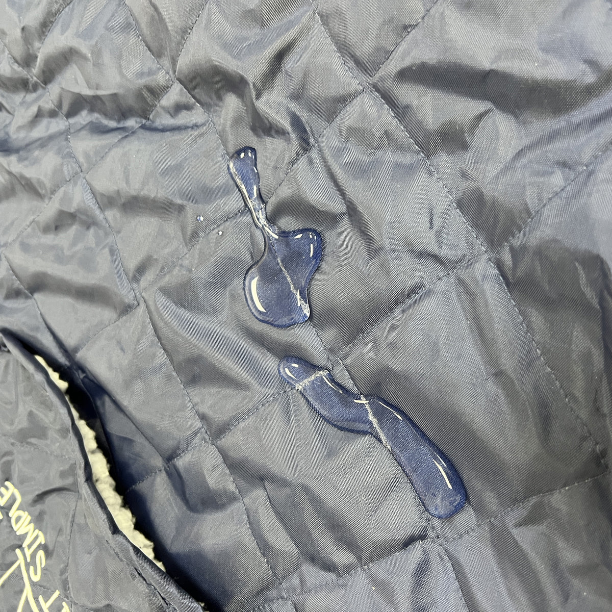 Water droplets bead up on the dark blue Waterproof Sherpa Blanket by Pro Towels, highlighting its water-resistant properties and distinctive square-stitched quilting.