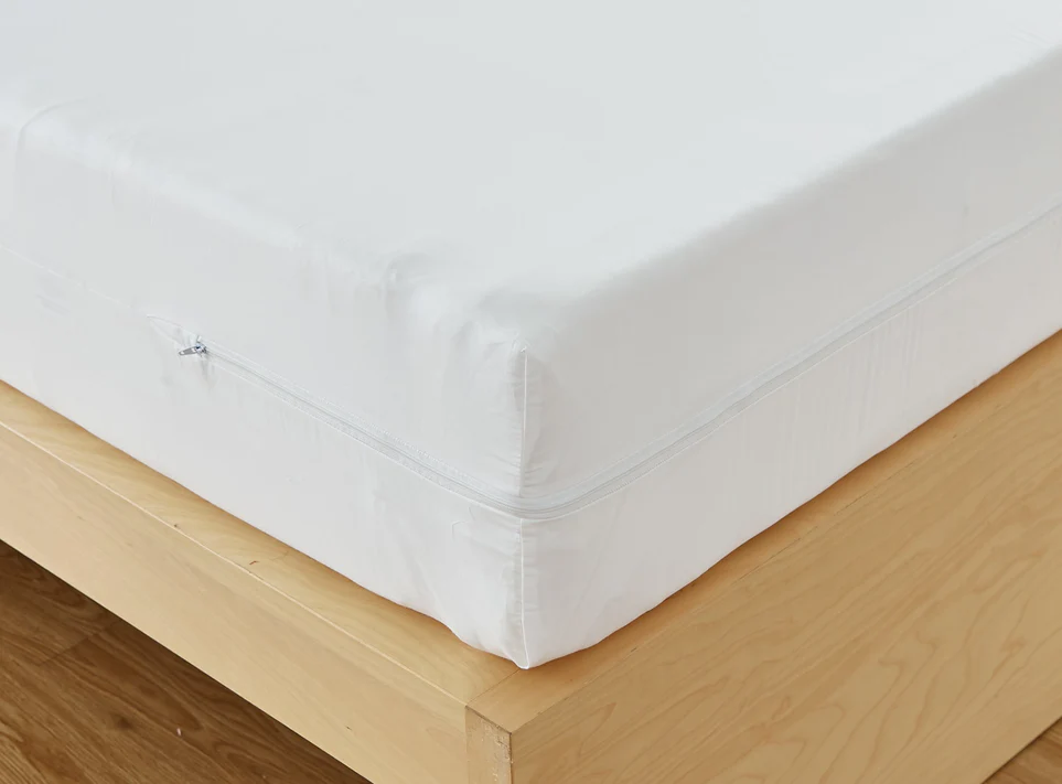 A close-up of a mattress on a light wooden bed frame features the Bargoose AllergyCare Cotton Zippered Mattress Encasement - 16 Deep, providing added bed bug protection with its white cotton cover.