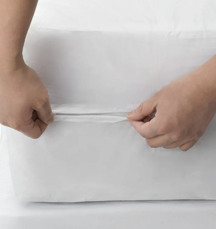 Close-up of two hands unzipping a Bargoose AllergyCare Cotton Zippered Mattress Encasement - 9 Deep, revealing the zipper and part of the mattress beneath.
