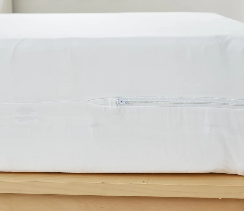 A close-up of the Bargoose AllergyCare Cotton Zippered Mattress Encasement (16 Deep) shows its fitted design and visible side zipper, providing added bed bug protection on a light wooden bed frame.