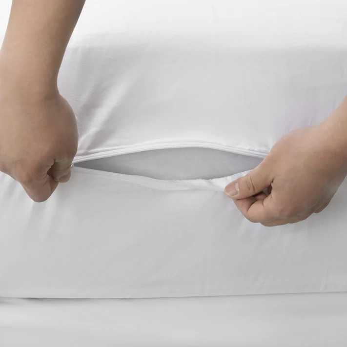 Close-up of two hands opening a hidden zipper on the side of a Bargoose AllergyCare Cotton Zippered Mattress Encasement - 9 Deep, revealing the mattress inside.