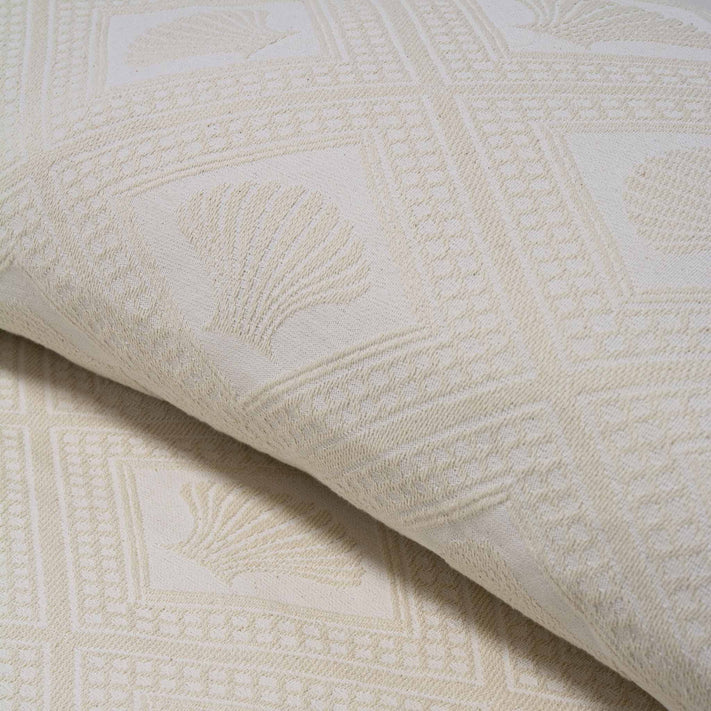 Close-up of the Avalon Jacquard Bedspread by Bargoose, featuring cream-colored fabric with raised seashells in squares and geometric borders—its intricate woven design is perfect for hotel bedding.