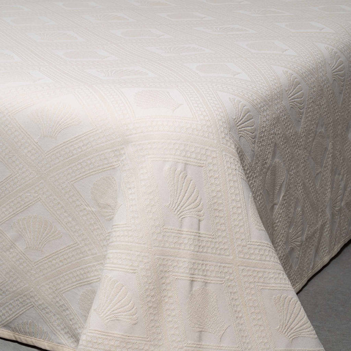 A close-up view of the cream Avalon Jacquard Bedspread by Bargoose, featuring a textured geometric pattern with embroidered seashells—an elegant choice for upgrading hotel bedding.