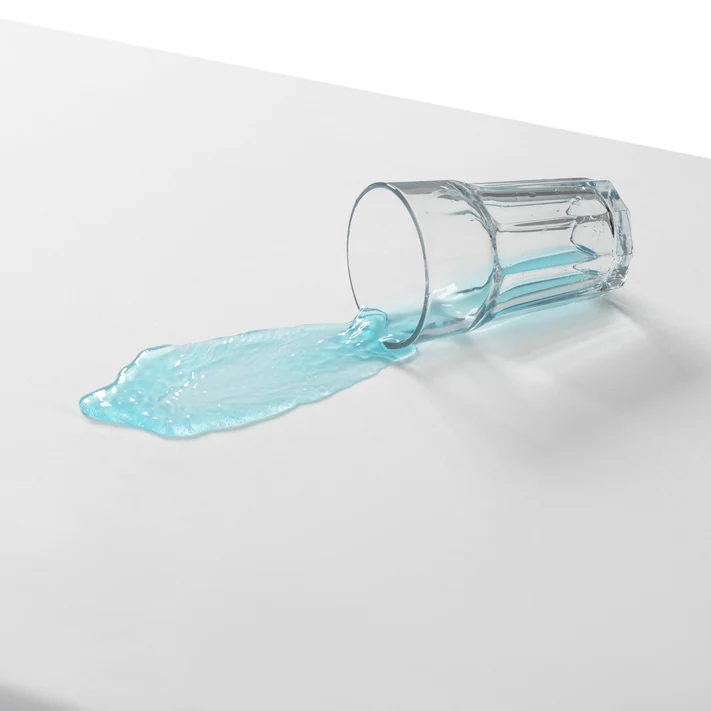 A clear glass spills blue liquid onto a white surface—exactly the mess the Bargoose 6 Gauge Vinyl Fitted Waterproof Mattress Cover (9 deep) helps prevent.