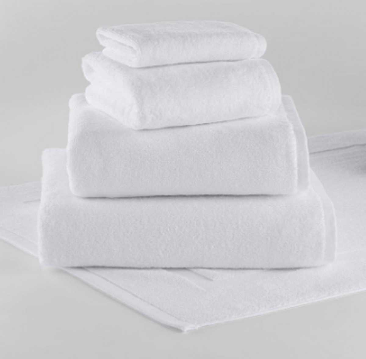A plush 1Concier Wash Cloth from the Silver Terry Collection, crafted from 100% cotton, is neatly displayed on a matching white bath mat against a plain light background.