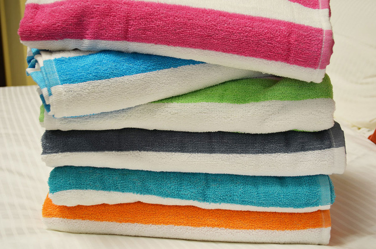 A stack of five Ganesh Mills Promotional Beach Towels - Assorted Cabana Stripe with white edges and colorful stripes in pink, blue, green, gray, and orange is neatly folded on a white surface.