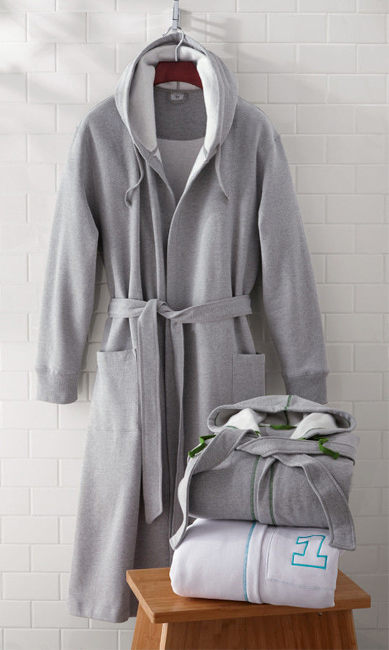 A gray microfiber terry robe by 1Concier hangs on a hook against a white tiled wall. Two folded Belts Boxer Belts by 1Concier, featuring green and blue trim with a number 1 embroidered, rest on a wooden bench.